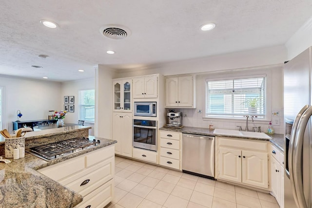 kitchen with plenty of natural light, appliances with stainless steel finishes, light stone counters, and a sink
