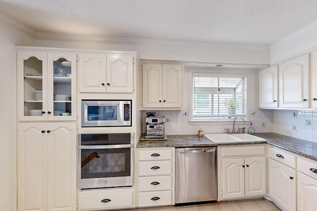 kitchen with tasteful backsplash, a sink, ornamental molding, appliances with stainless steel finishes, and dark countertops