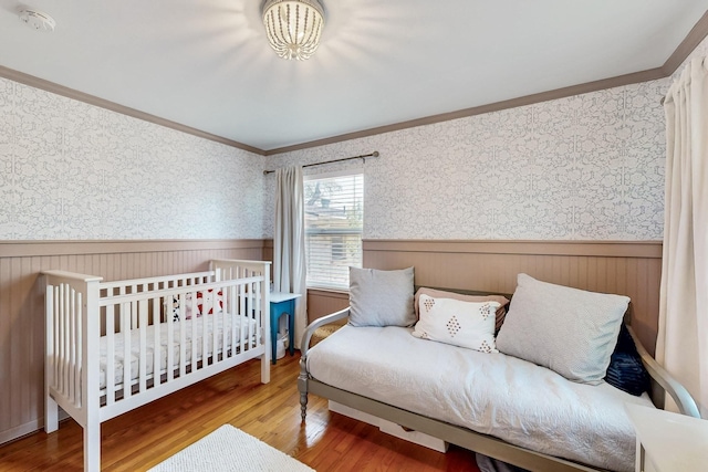 bedroom featuring wainscoting, wallpapered walls, wood finished floors, and ornamental molding