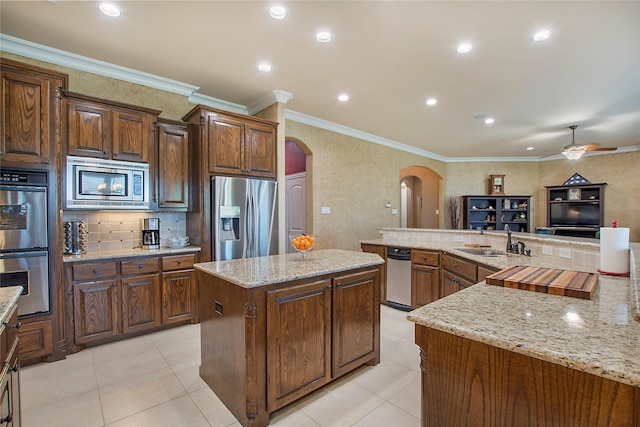 kitchen featuring appliances with stainless steel finishes, a large island, decorative backsplash, arched walkways, and a sink