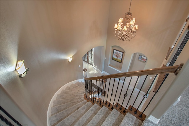 stairway featuring a towering ceiling, a notable chandelier, baseboards, carpet flooring, and arched walkways
