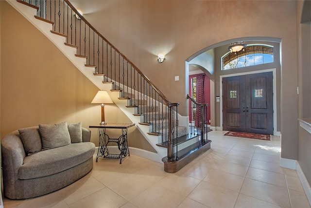 entrance foyer with arched walkways, baseboards, tile patterned flooring, and stairway