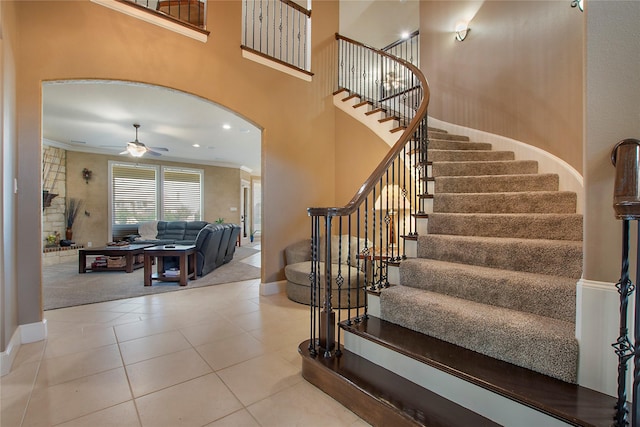 stairs with a towering ceiling, baseboards, ornamental molding, tile patterned flooring, and ceiling fan