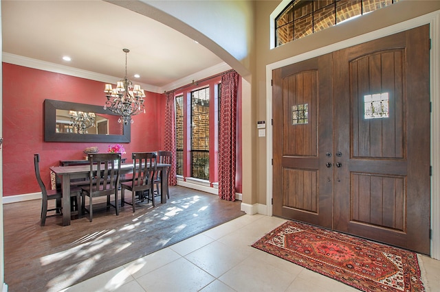 foyer with ornamental molding, baseboards, arched walkways, and a notable chandelier