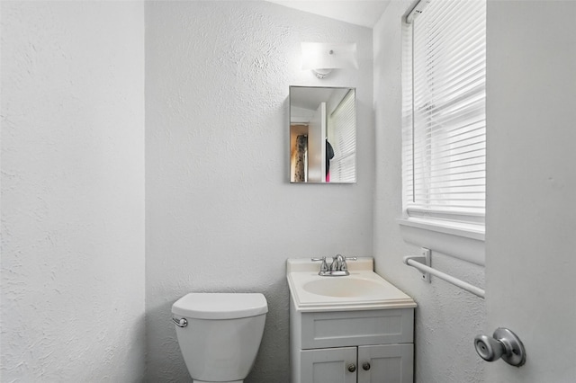 bathroom featuring toilet, a textured wall, and vanity