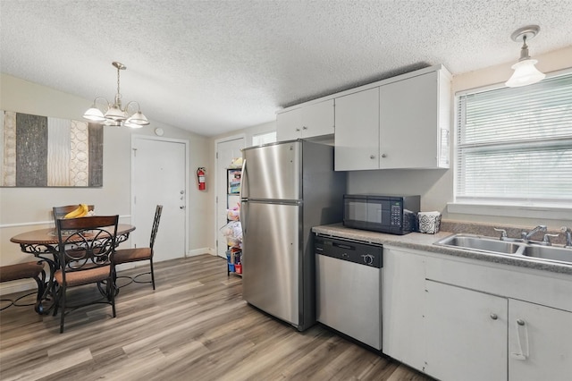 kitchen featuring a textured ceiling, appliances with stainless steel finishes, a sink, light wood finished floors, and an inviting chandelier
