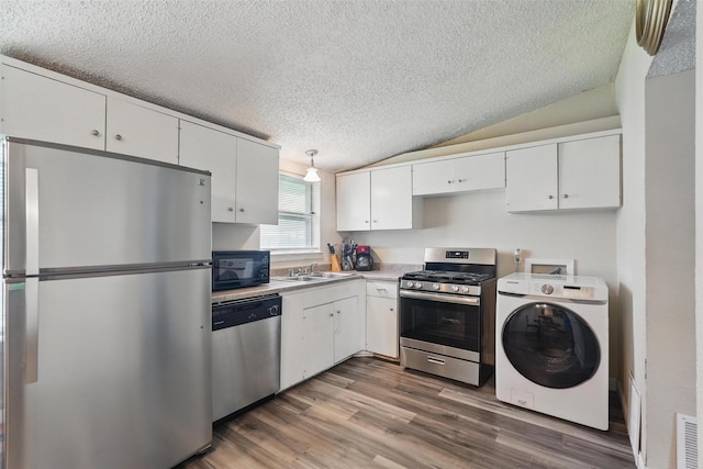kitchen featuring a textured ceiling, wood finished floors, washer / dryer, stainless steel appliances, and white cabinetry