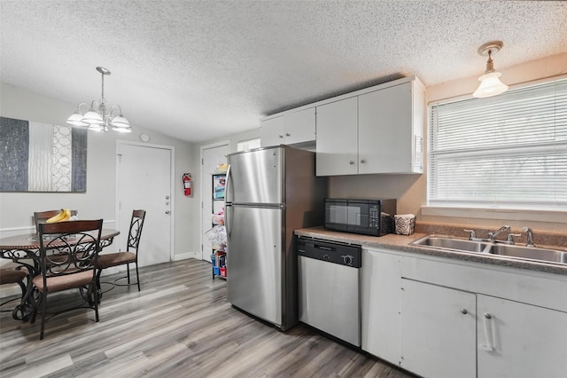kitchen with a textured ceiling, a sink, light wood finished floors, vaulted ceiling, and stainless steel appliances