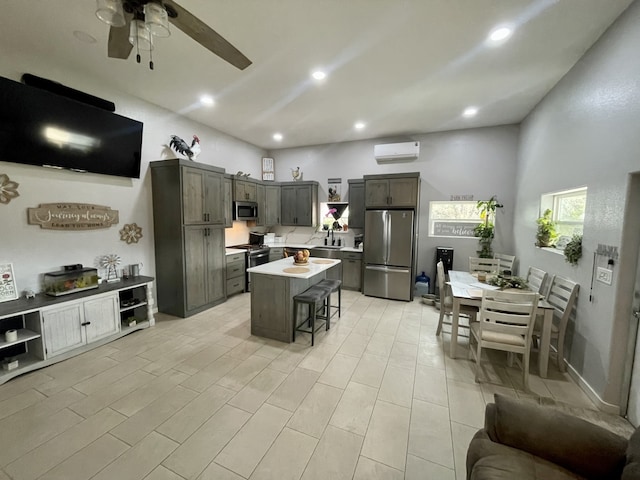 kitchen featuring a wall mounted AC, light countertops, stainless steel appliances, a ceiling fan, and a kitchen breakfast bar