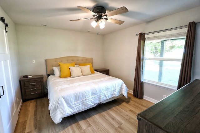 2432 Cottondale Rd, Springtown, TX 76082 - bedroom featuring a barn door, baseboards, light wood-style flooring, and ceiling fan