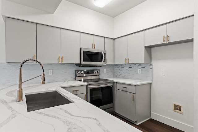 kitchen with tasteful backsplash, light stone counters, appliances with stainless steel finishes, a sink, and baseboards