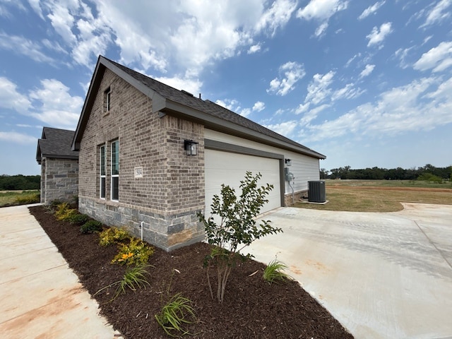 504 Ashlow Ct, Springtown, TX 76082 - view of home's exterior featuring concrete driveway, central AC, stone siding, an attached garage, and brick siding