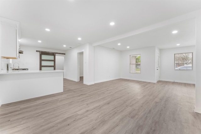 11534 Fernald Ave, Dallas, TX 75218 - unfurnished living room with a barn door, light wood-style floors, recessed lighting, baseboards, and a sink
