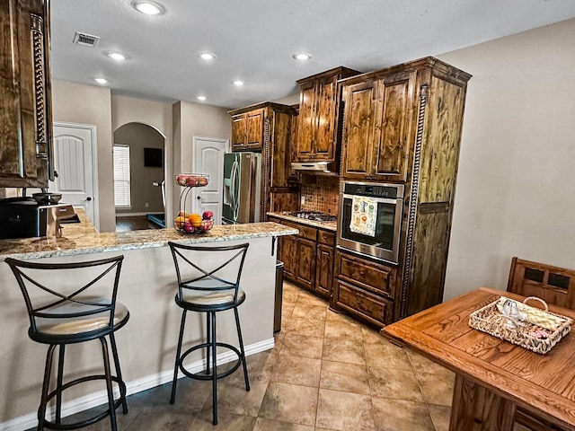 300 Cleve Cole Rd, Denison, TX 75021 - kitchen with appliances with stainless steel finishes, arched walkways, under cabinet range hood, a peninsula, and a kitchen breakfast bar