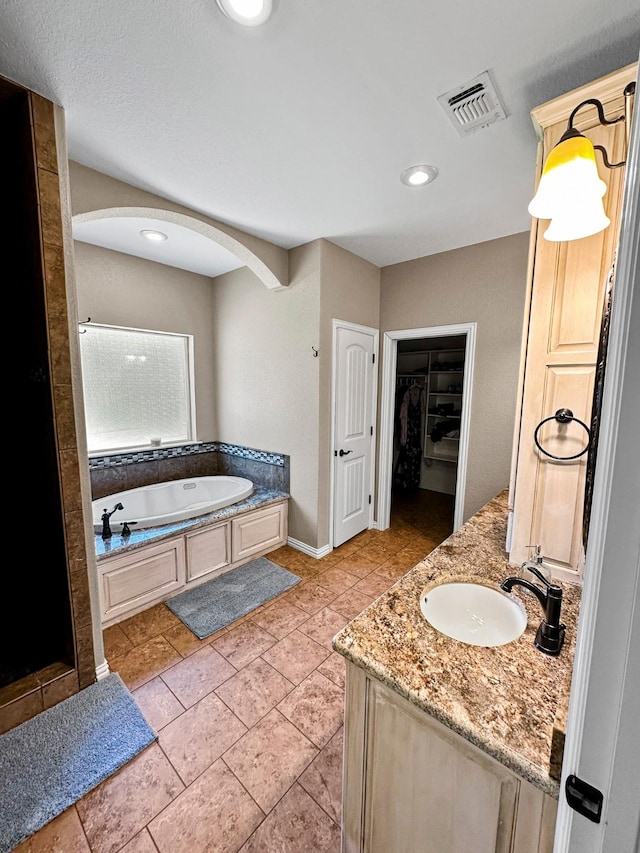 bathroom featuring a spacious closet, a bath, vanity, baseboards, and tile patterned floors