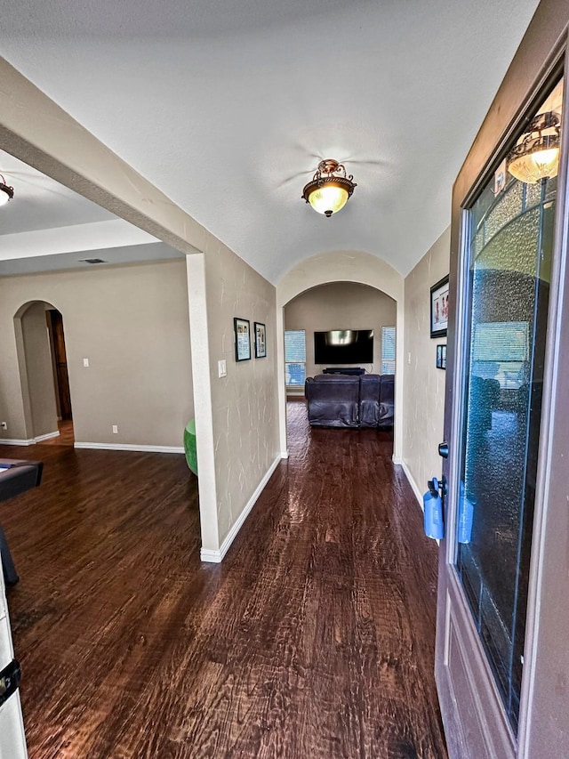 hallway with arched walkways, wood finished floors, baseboards, and vaulted ceiling