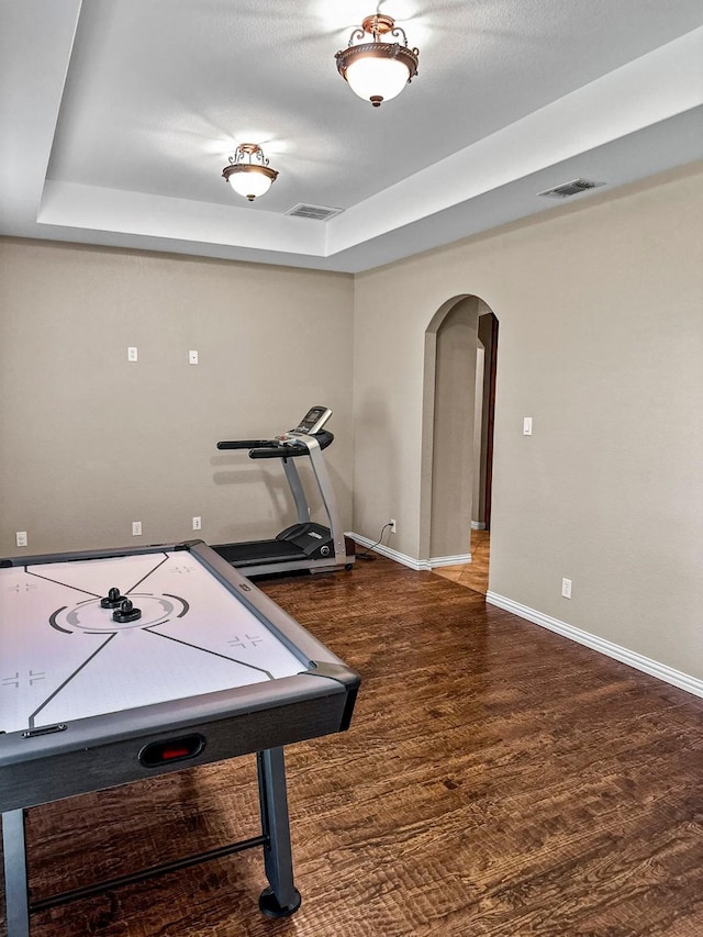 recreation room featuring arched walkways, wood finished floors, a tray ceiling, and baseboards