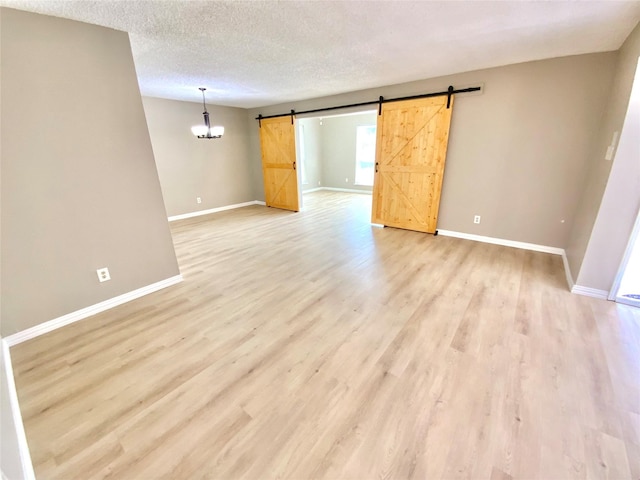 1332 Burmeister Rd, Fort Worth, TX 76134 - empty room featuring baseboards, a textured ceiling, a barn door, light wood finished floors, and a notable chandelier