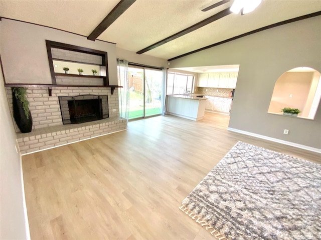 1332 Burmeister Rd, Fort Worth, TX 76134 - unfurnished living room featuring a ceiling fan, vaulted ceiling with beams, a fireplace, a textured ceiling, and light wood-type flooring