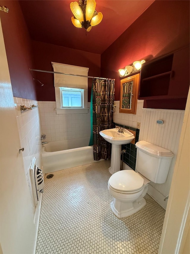 bathroom featuring tile patterned floors, wainscoting, tile walls, shower / bath combo, and toilet