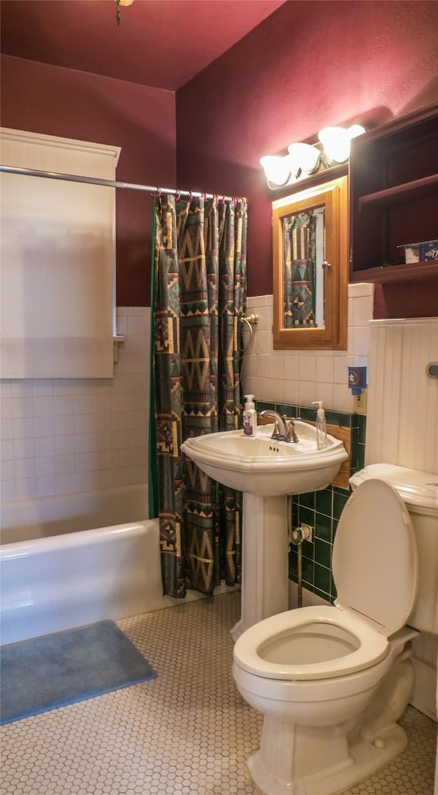 bathroom featuring tile patterned flooring, shower / bath combination with curtain, tile walls, a wainscoted wall, and toilet