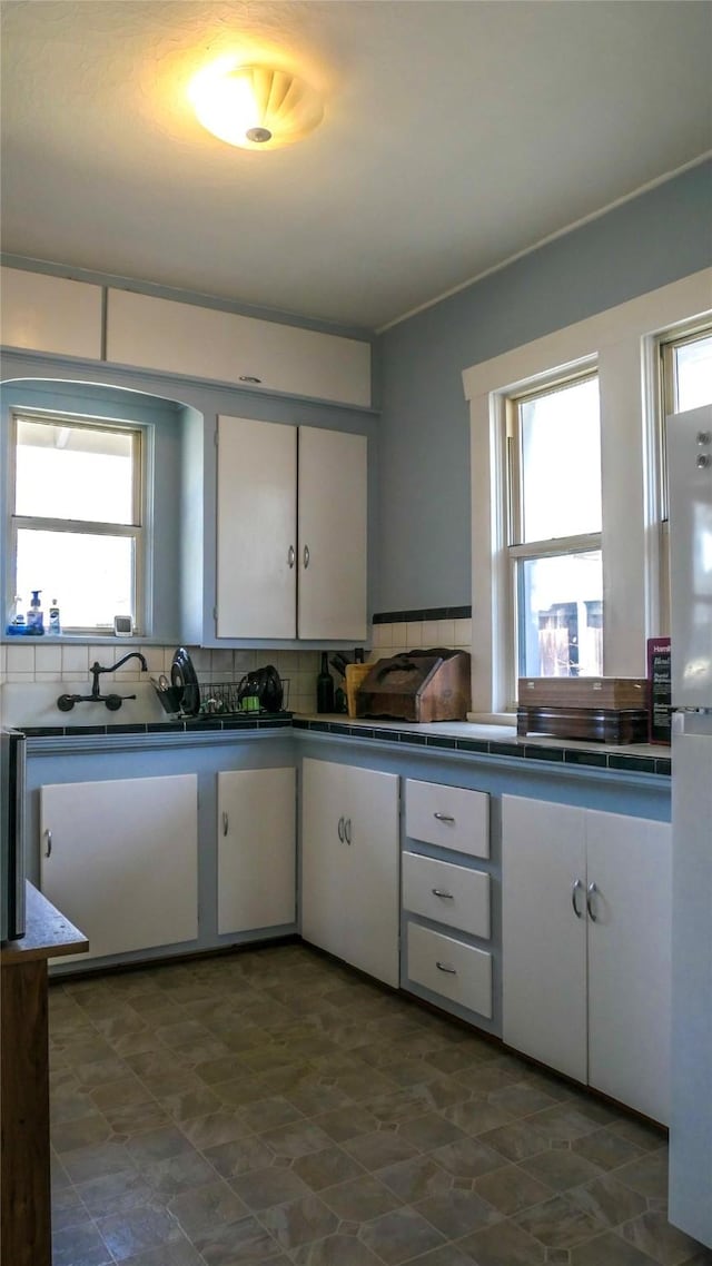 kitchen with tile counters, white cabinets, freestanding refrigerator, and tasteful backsplash