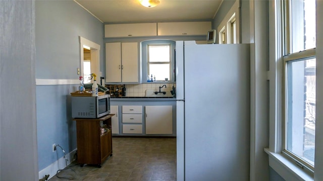 kitchen with stainless steel microwave, backsplash, ornamental molding, dark countertops, and freestanding refrigerator