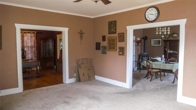 unfurnished room featuring crown molding, a wood stove, baseboards, carpet, and ceiling fan with notable chandelier