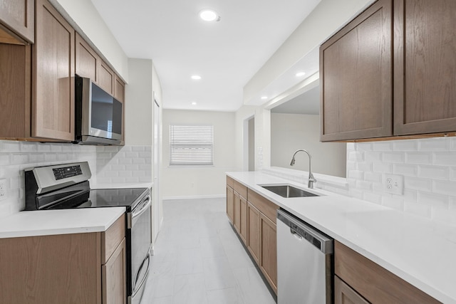 kitchen with recessed lighting, stainless steel appliances, a sink, baseboards, and decorative backsplash