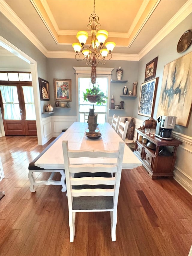 dining space with a tray ceiling, wood finished floors, an inviting chandelier, and a decorative wall