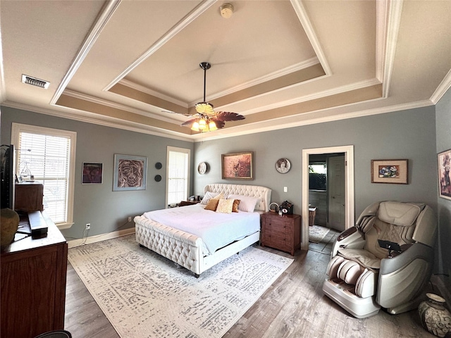 bedroom featuring a tray ceiling, wood finished floors, ornamental molding, and multiple windows