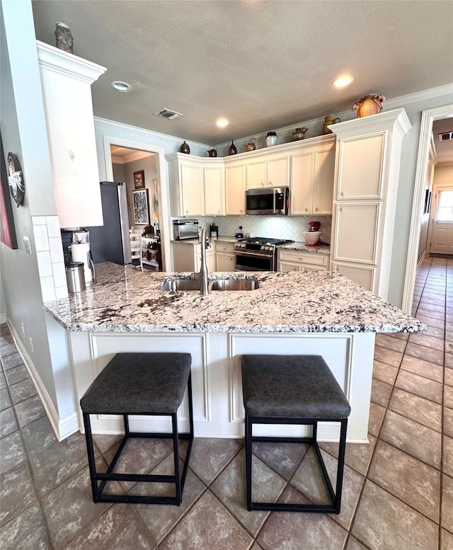 kitchen with a peninsula, crown molding, a kitchen bar, stainless steel appliances, and a sink