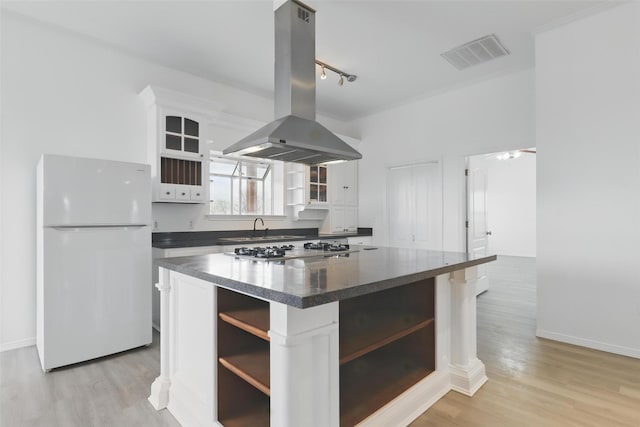 kitchen featuring open shelves, island exhaust hood, dark countertops, visible vents, and freestanding refrigerator