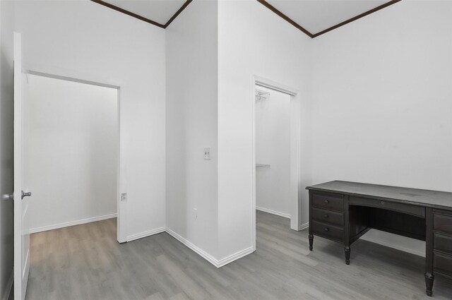interior space with baseboards, wood finished floors, ornamental molding, and a walk in closet