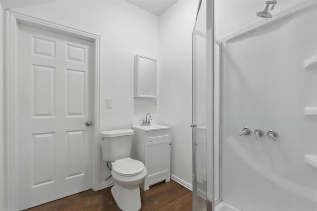 bathroom with a shower stall, baseboards, wood finished floors, toilet, and a sink