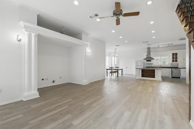 unfurnished living room featuring light wood-type flooring, visible vents, decorative columns, and ceiling fan with notable chandelier