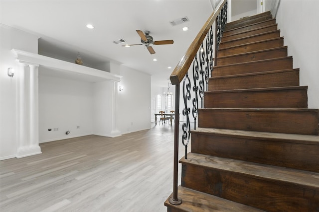staircase featuring visible vents, wood finished floors, ceiling fan, and ornate columns