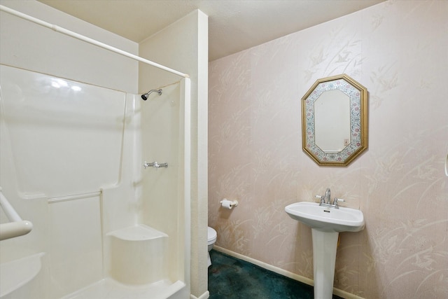 bathroom featuring toilet, baseboards, wallpapered walls, a sink, and walk in shower