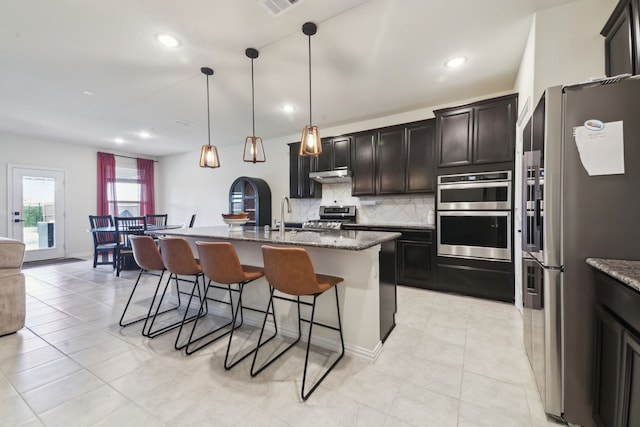 342 Meredith Dr, Fate, TX 75087 - kitchen featuring appliances with stainless steel finishes, under cabinet range hood, a kitchen bar, tasteful backsplash, and dark stone countertops