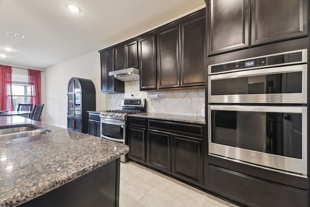 342 Meredith Dr, Fate, TX 75087 - kitchen with stainless steel appliances, under cabinet range hood, tasteful backsplash, arched walkways, and dark stone countertops