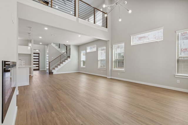 4516 Rustic Ridge Dr, Mckinney, TX 75071 - unfurnished living room featuring light wood finished floors, stairway, a high ceiling, a chandelier, and recessed lighting