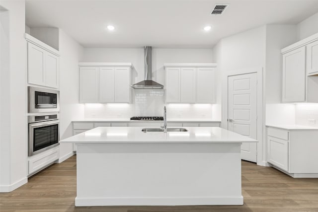 4516 Rustic Ridge Dr, Mckinney, TX 75071 - kitchen featuring stainless steel oven, wall chimney range hood, built in microwave, decorative backsplash, and a kitchen island with sink