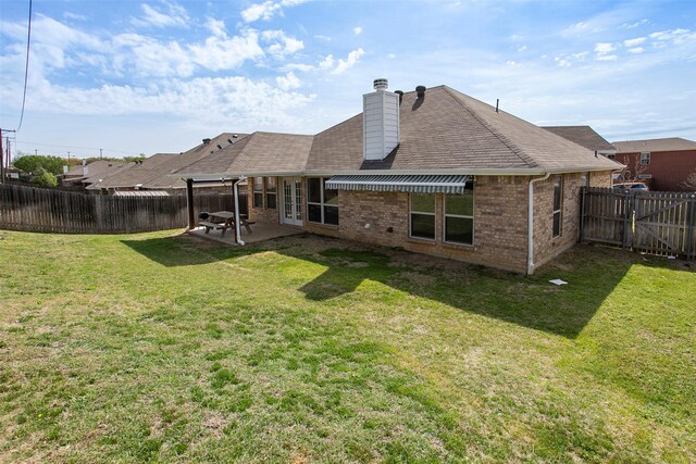 rear view of property with a patio area, a lawn, a fenced backyard, brick siding, and french doors