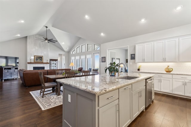 kitchen featuring a tile fireplace, a sink, a ceiling fan, dishwasher, and dark wood-style floors