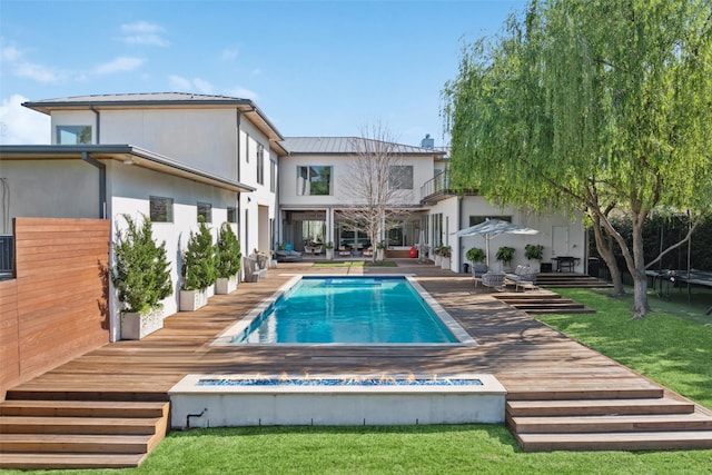 rear view of property with an outdoor pool, a trampoline, a yard, and stucco siding