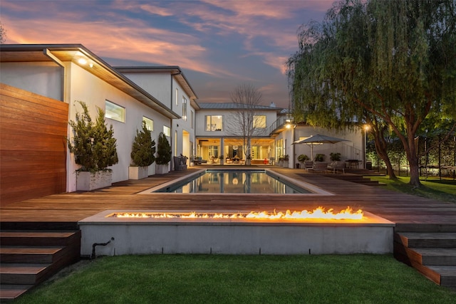 rear view of house with stucco siding, an outdoor pool, an outdoor fire pit, a yard, and a deck