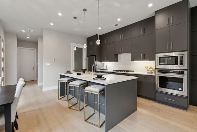 2228 Wycliff Ave, Dallas, TX 75219 - kitchen with light countertops, visible vents, light wood finished floors, a center island with sink, and appliances with stainless steel finishes