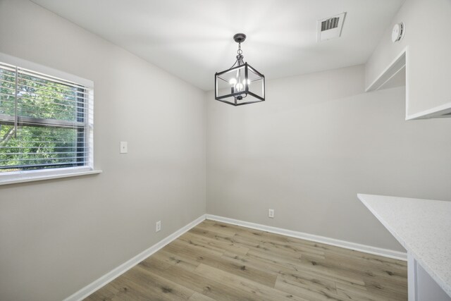 unfurnished dining area featuring light wood finished floors, baseboards, visible vents, and an inviting chandelier