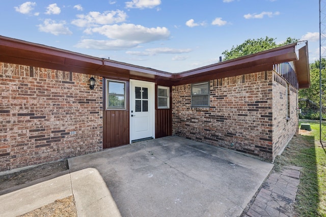 property entrance featuring brick siding, a patio, and board and batten siding