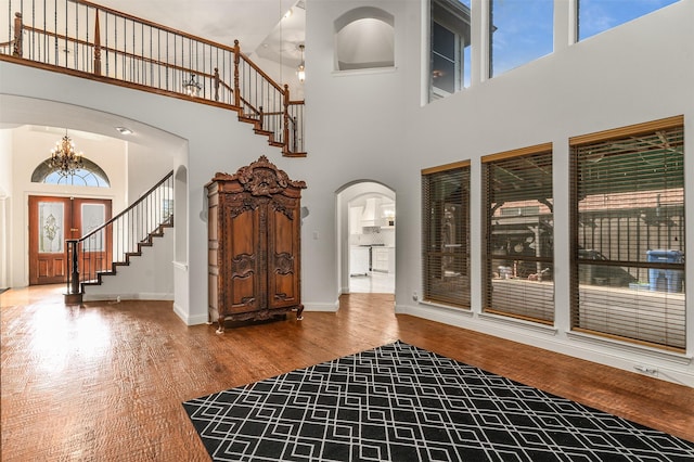 foyer entrance featuring arched walkways, an inviting chandelier, a healthy amount of sunlight, and a towering ceiling